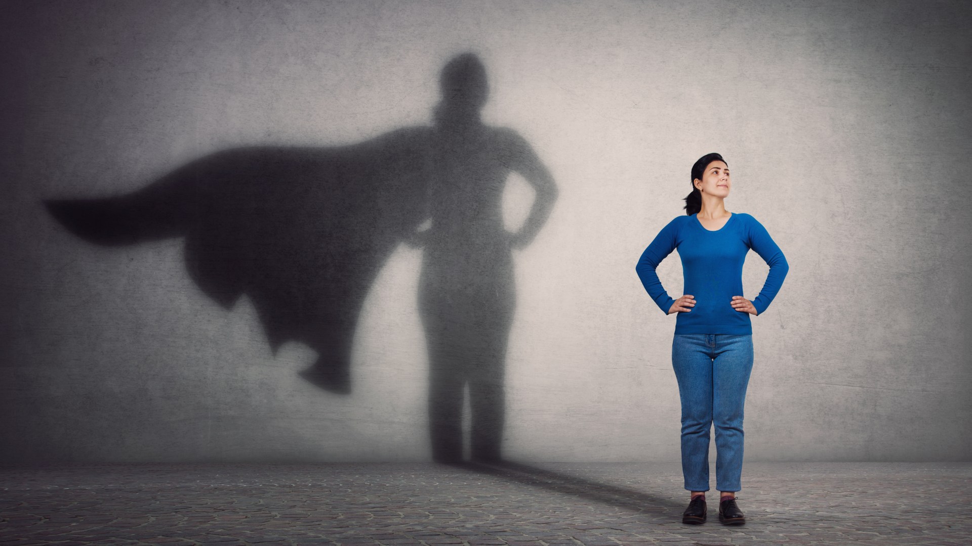 woman standing with hands on hips, her shadow wearing a cape in the background, your achievement